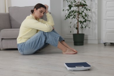 Photo of Depressed woman and scales on floor at home, selective focus. Bulimia problem