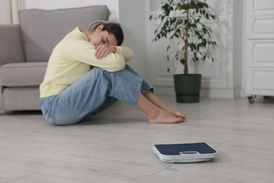 Photo of Depressed woman and scales on floor at home, selective focus. Bulimia problem