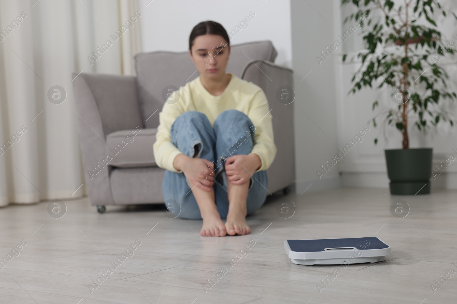 Photo of Depressed woman and scales on floor at home, selective focus. Bulimia problem