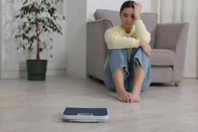 Photo of Depressed woman and scales on floor at home, selective focus with space for text. Bulimia problem