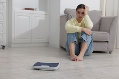 Photo of Depressed woman and scales on floor at home, selective focus with space for text. Bulimia problem