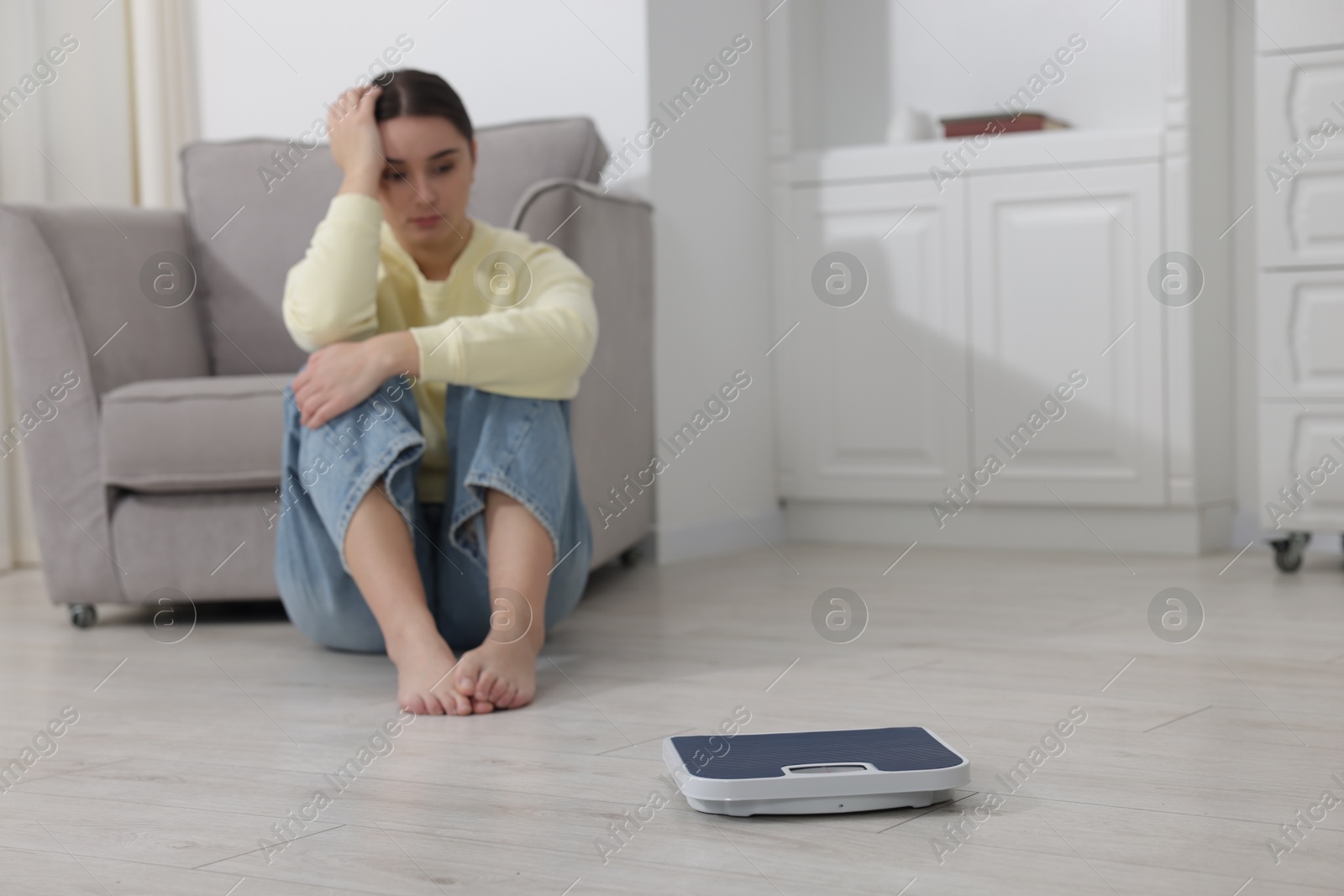 Photo of Depressed woman and scales on floor at home, selective focus with space for text. Bulimia problem