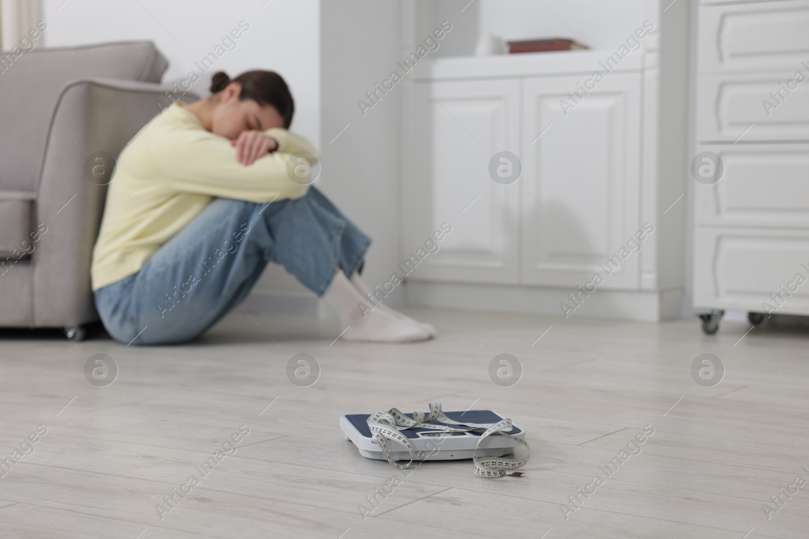 Photo of Depressed woman, scales and measuring tape on floor at home, selective focus with space for text. Bulimia problem