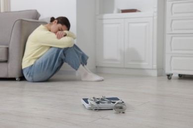 Photo of Depressed woman, scales and measuring tape on floor at home, selective focus with space for text. Bulimia problem