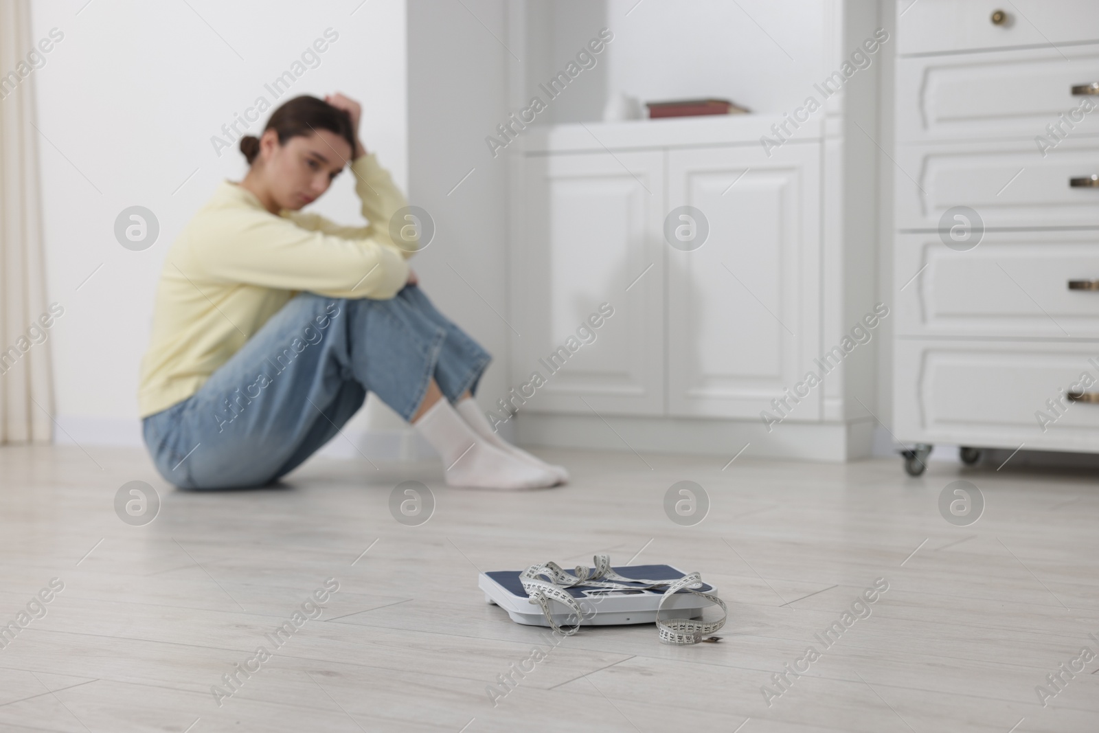 Photo of Depressed woman, scales and measuring tape on floor at home, selective focus with space for text. Bulimia problem