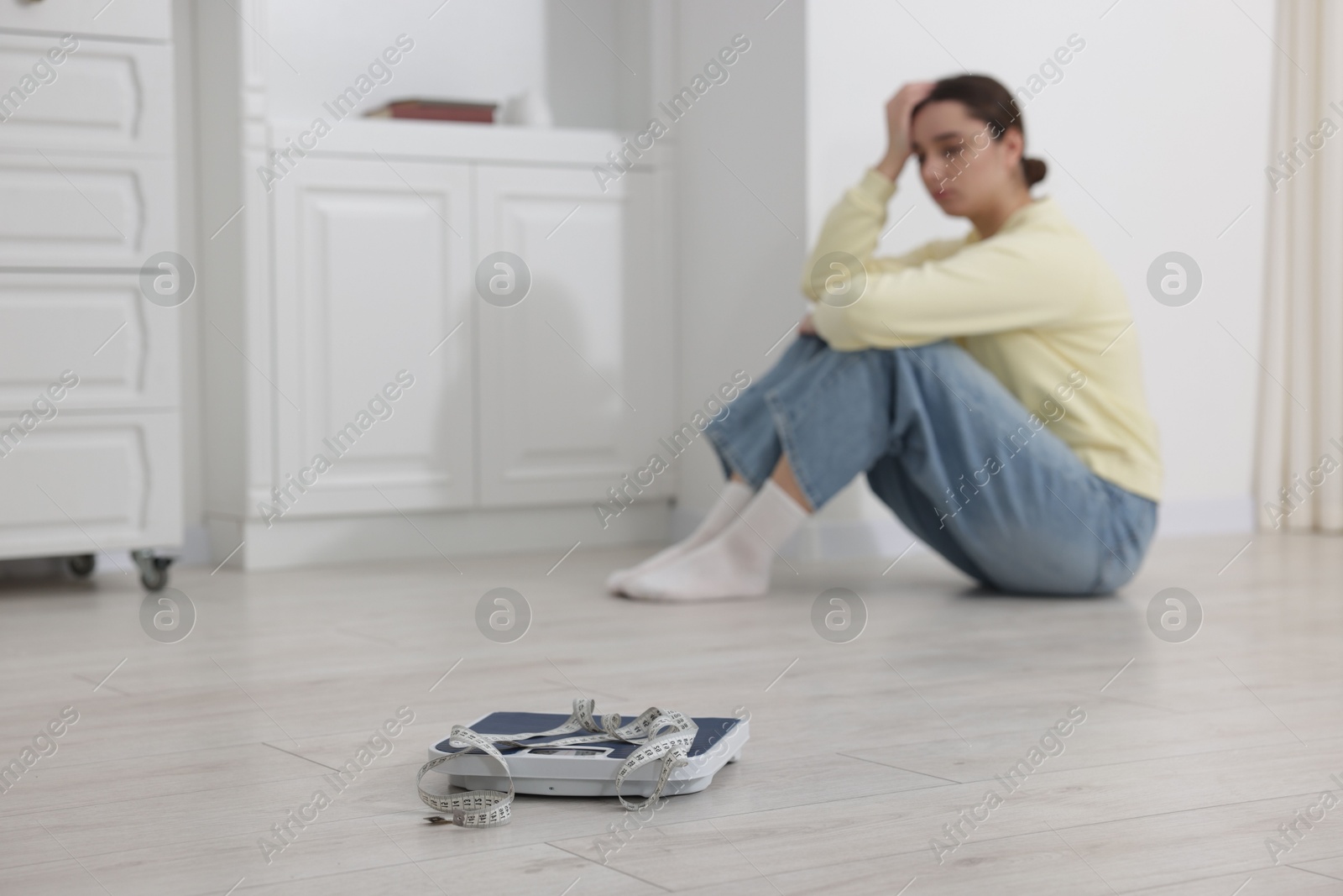 Photo of Depressed woman, scales and measuring tape on floor at home, selective focus with space for text. Bulimia problem