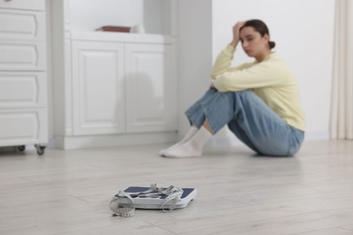 Photo of Depressed woman, scales and measuring tape on floor at home, selective focus with space for text. Bulimia problem