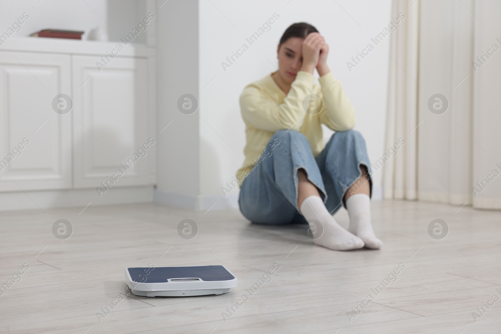 Photo of Depressed woman and scales on floor at home, selective focus with space for text. Bulimia problem