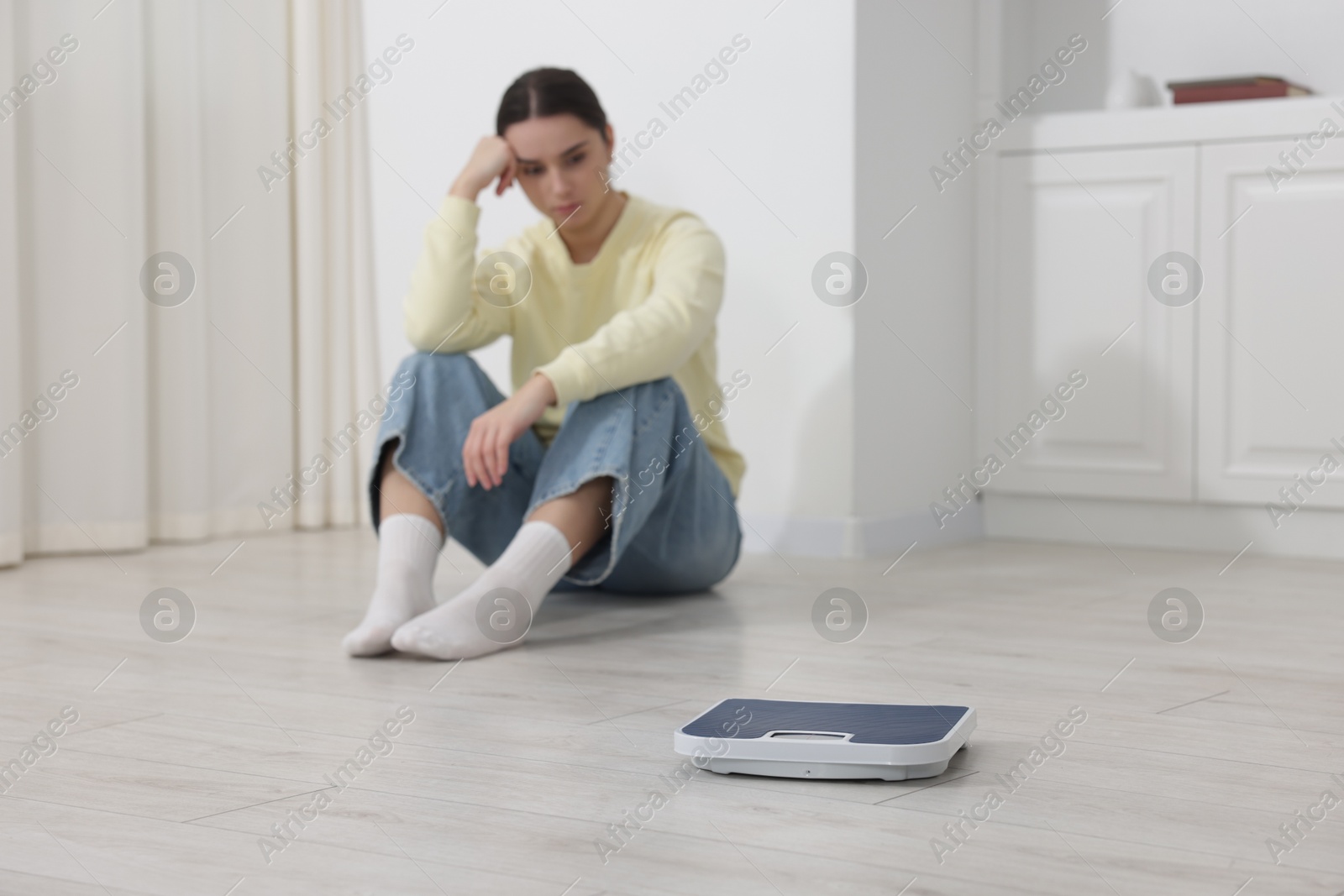 Photo of Depressed woman and scales on floor at home, selective focus with space for text. Bulimia problem