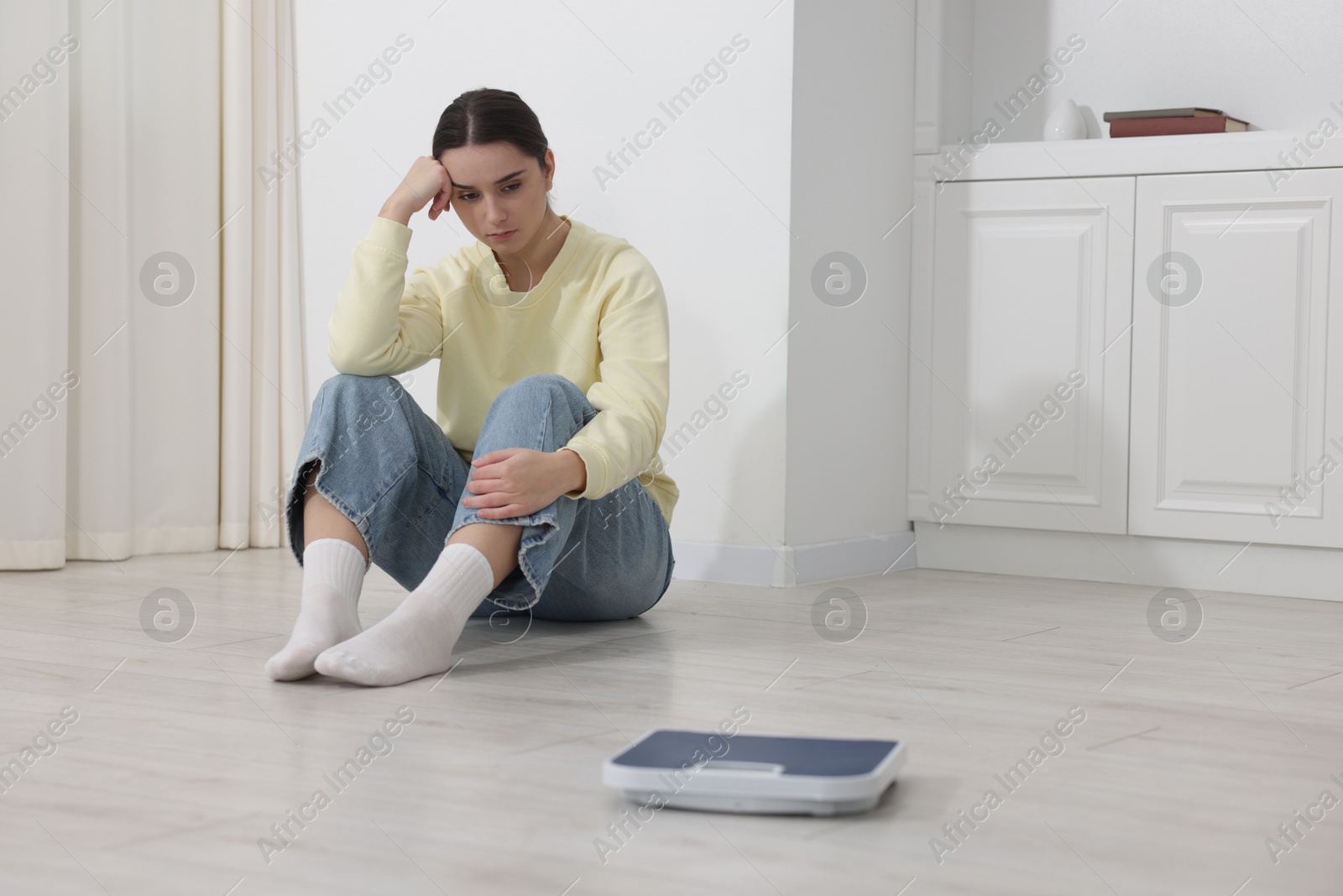 Photo of Depressed woman and scales on floor at home, selective focus with space for text. Bulimia problem