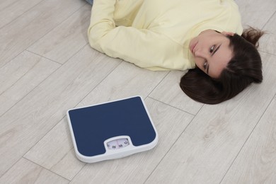 Photo of Depressed woman with scales lying on floor at home. Bulimia problem