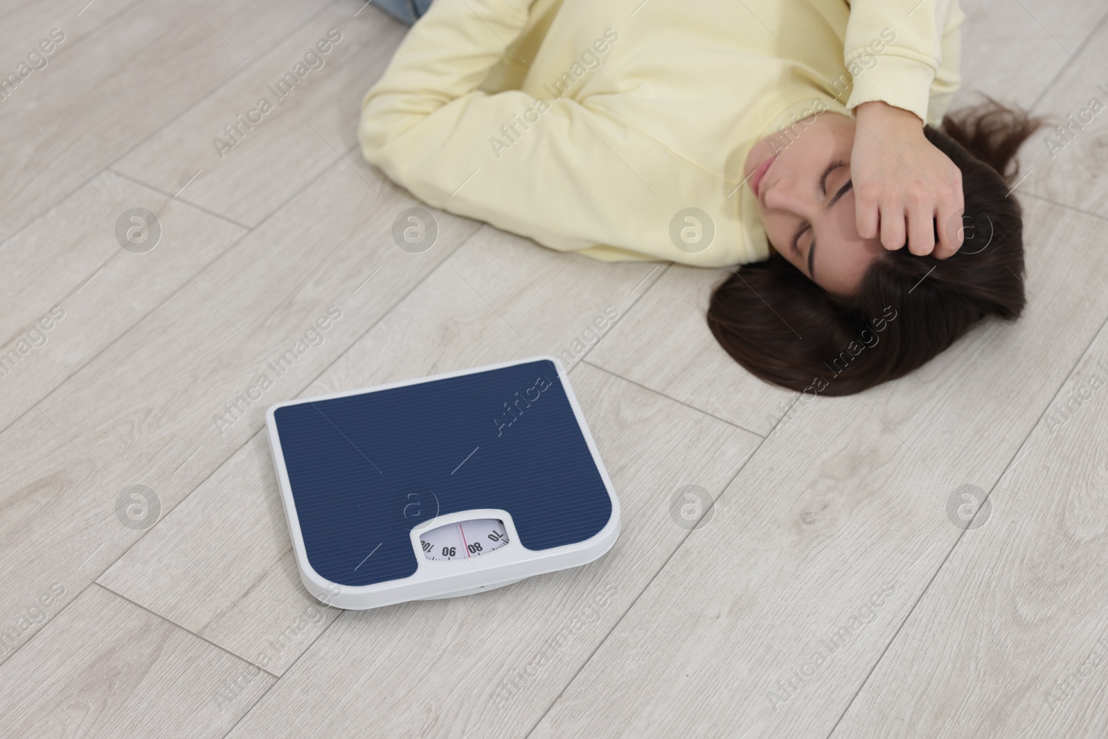 Photo of Depressed woman with scales lying on floor at home. Bulimia problem