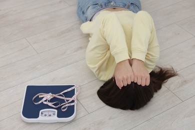 Photo of Depressed woman with scales and measuring tape lying on floor at home. Bulimia problem