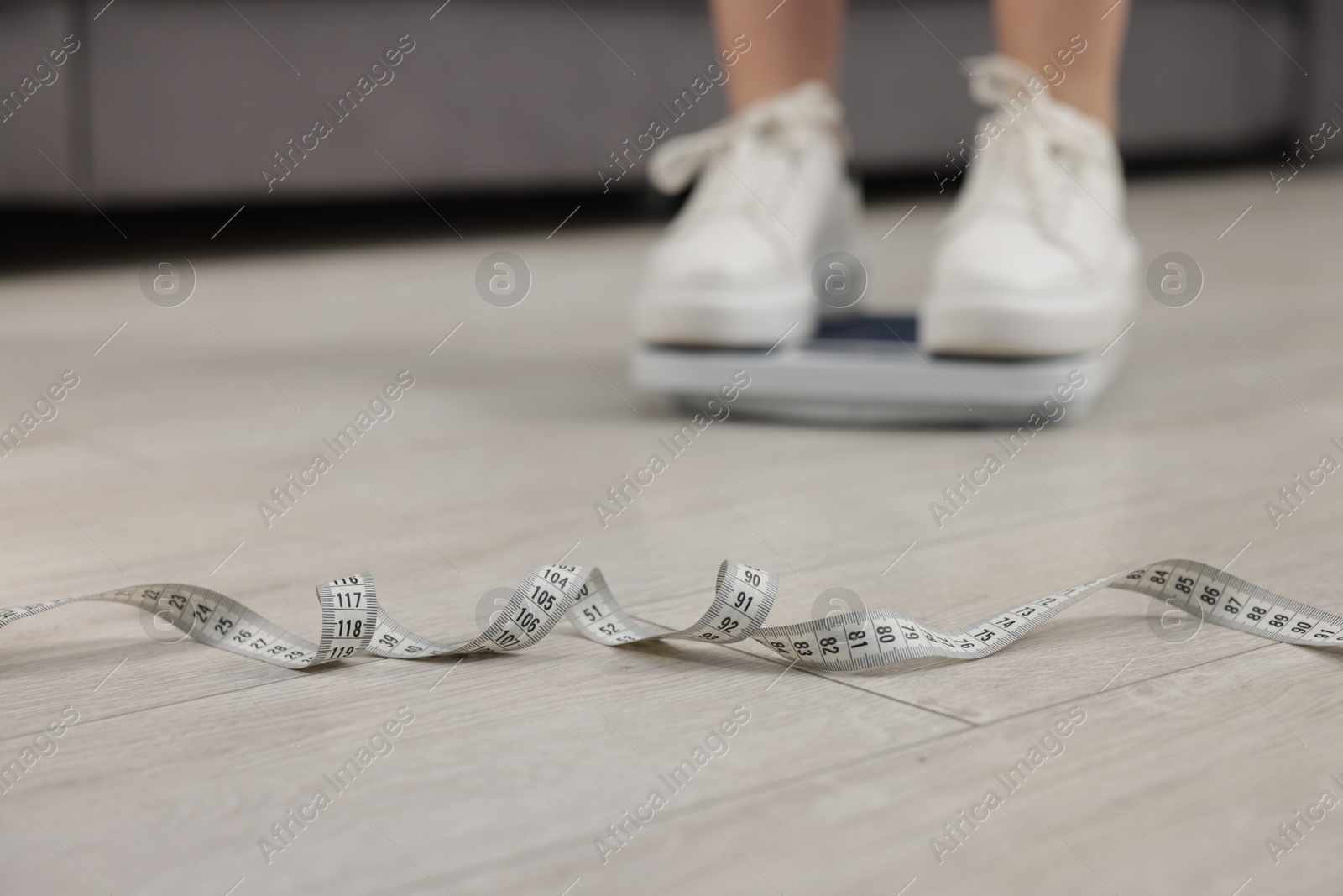 Photo of Woman on scales and measuring tape on floor indoors, selective focus. Weight loss