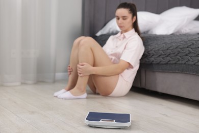 Photo of Depressed woman and scales on floor at home, selective focus. Bulimia problem