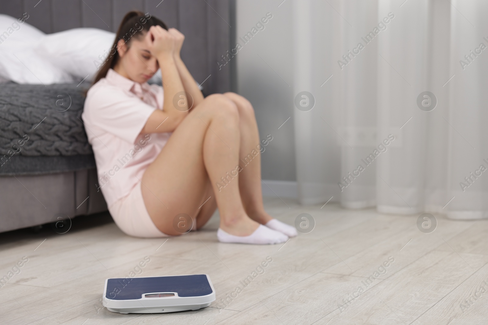 Photo of Depressed woman and scales on floor at home, selective focus with space for text. Bulimia problem