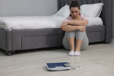 Photo of Depressed woman, scales and measuring tape on floor at home, selective focus with space for text. Bulimia problem