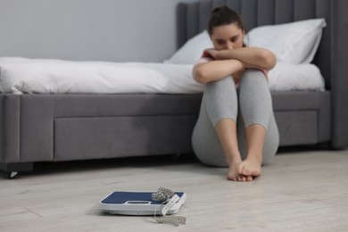 Photo of Depressed woman, scales and measuring tape on floor at home, selective focus with space for text. Bulimia problem