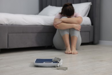 Photo of Depressed woman, scales and measuring tape on floor at home, selective focus with space for text. Bulimia problem