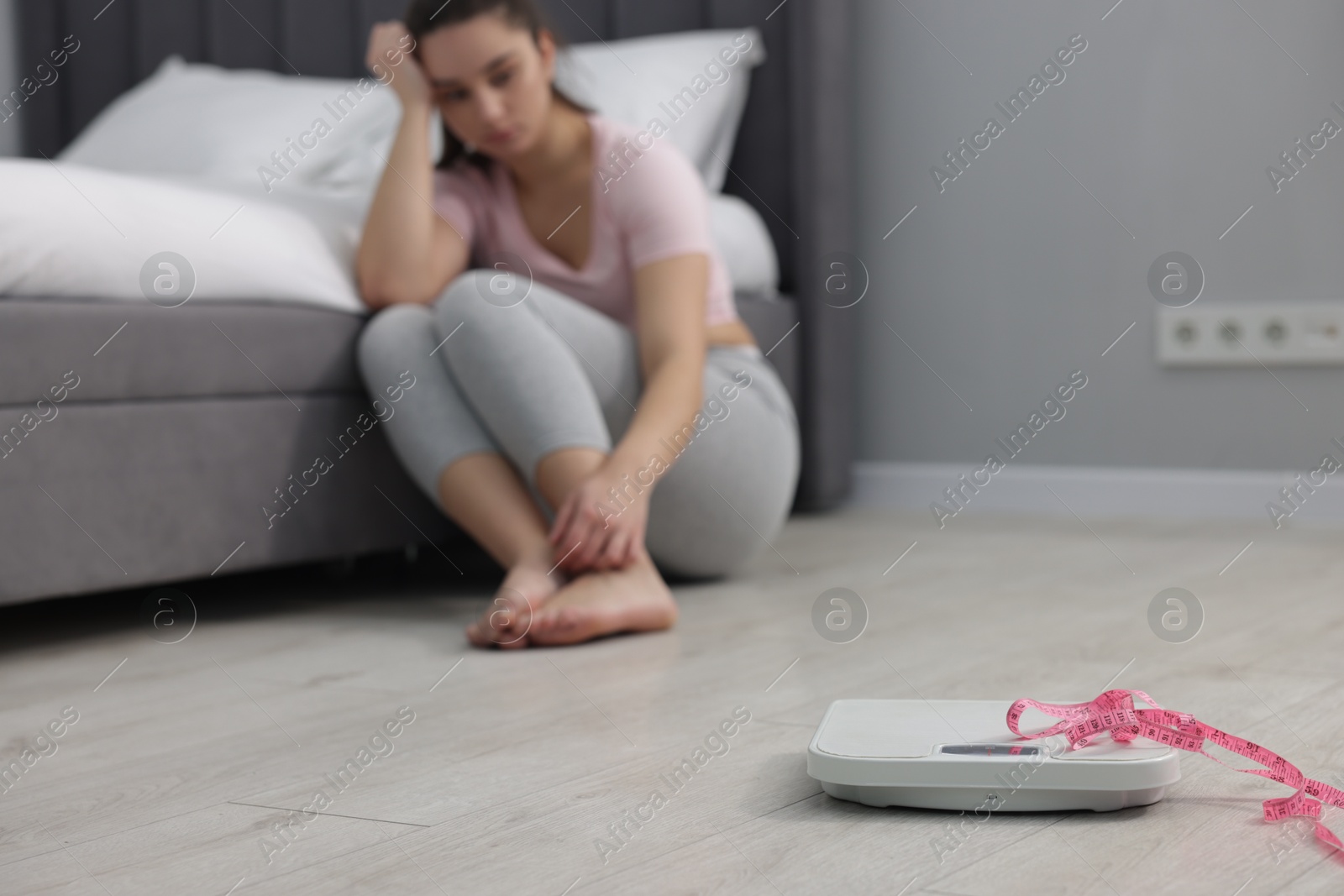 Photo of Depressed woman and scales with measuring tape on floor at home, selective focus. Bulimia problem