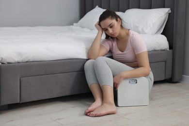 Photo of Depressed woman with scales on floor at home, space for text. Bulimia problem