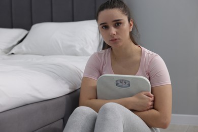 Photo of Depressed woman with scales on floor at home. Bulimia problem