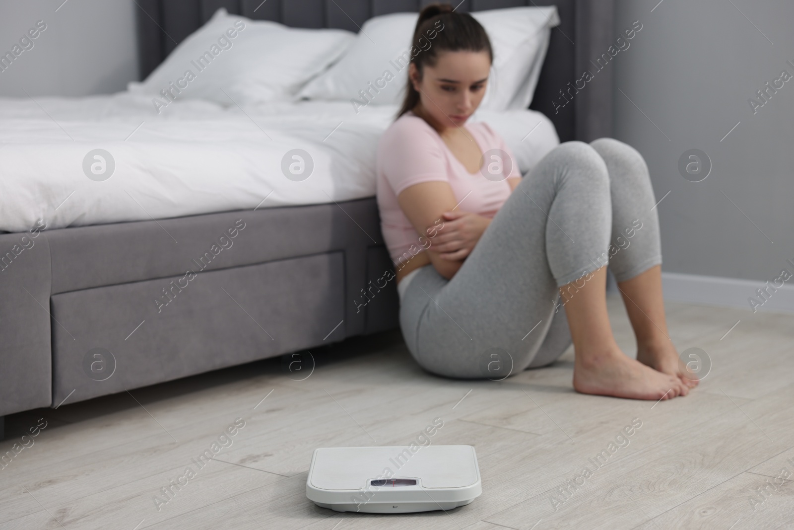 Photo of Depressed woman and scales on floor at home, selective focus with space for text. Bulimia problem