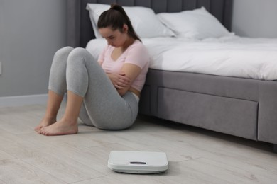 Photo of Depressed woman and scales on floor at home, selective focus with space for text. Bulimia problem