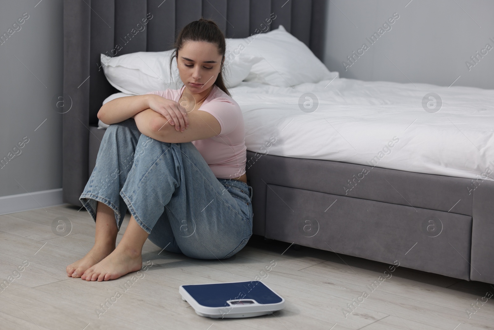 Photo of Depressed woman and scales on floor at home, space for text. Bulimia problem