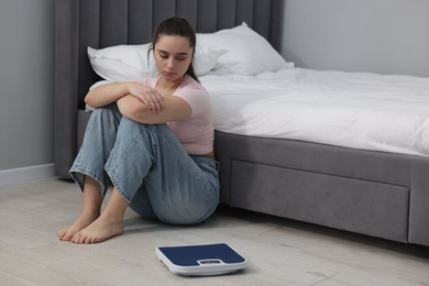 Photo of Depressed woman and scales on floor at home, space for text. Bulimia problem