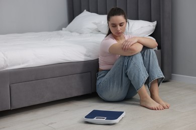 Photo of Depressed woman and scales on floor at home, space for text. Bulimia problem