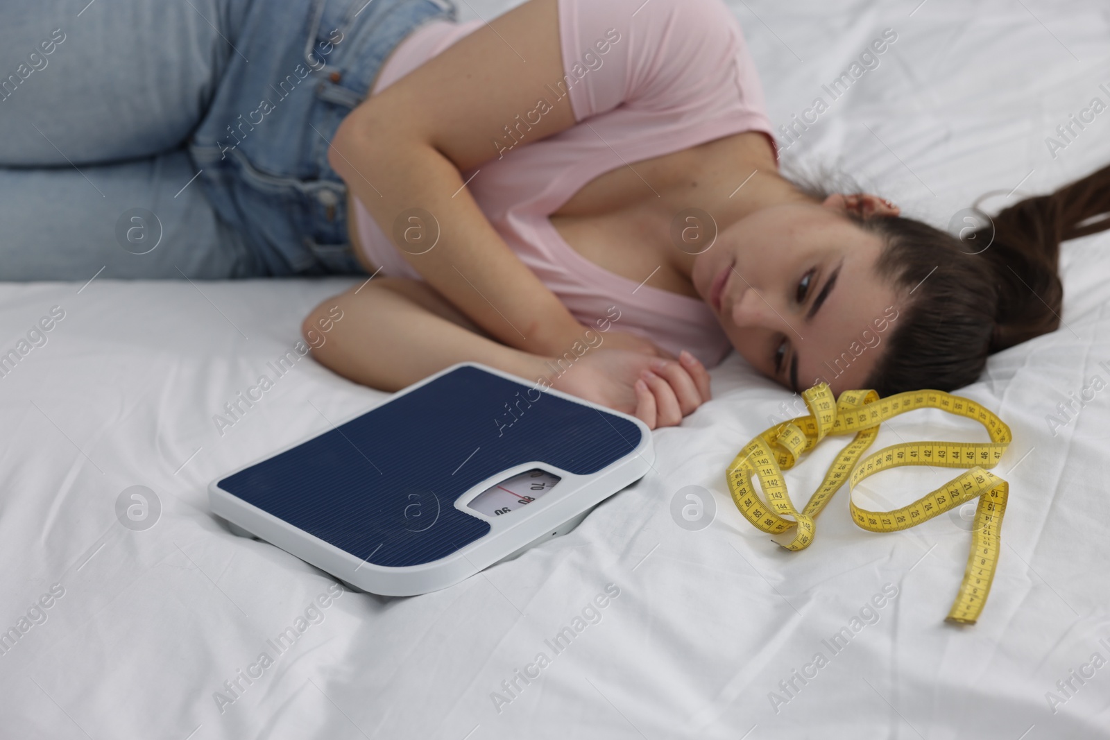 Photo of Depressed woman with scales and measuring tape on bed. Bulimia problem