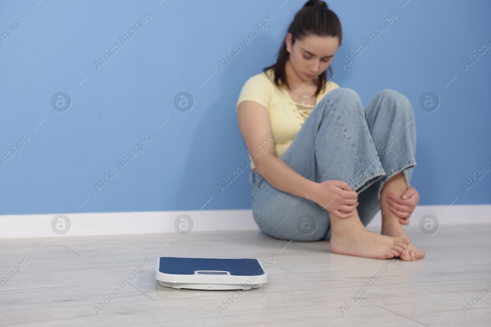 Photo of Depressed woman with scales on floor at home, space for text. Bulimia problem