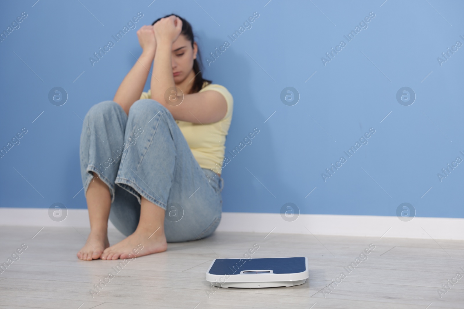 Photo of Depressed woman with scales on floor at home, space for text. Bulimia problem