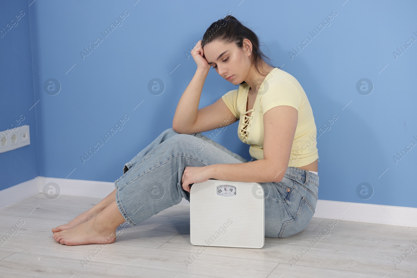 Photo of Depressed woman with scales on floor at home. Bulimia problem