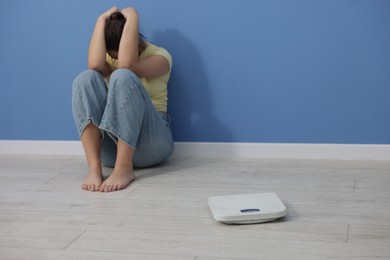 Photo of Depressed woman and scales on floor at home, space for text. Bulimia problem