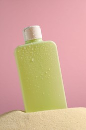 Bottle of sun protection product on sand against pink background