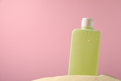 Photo of Bottle of sun protection product on sand against pink background, space for text