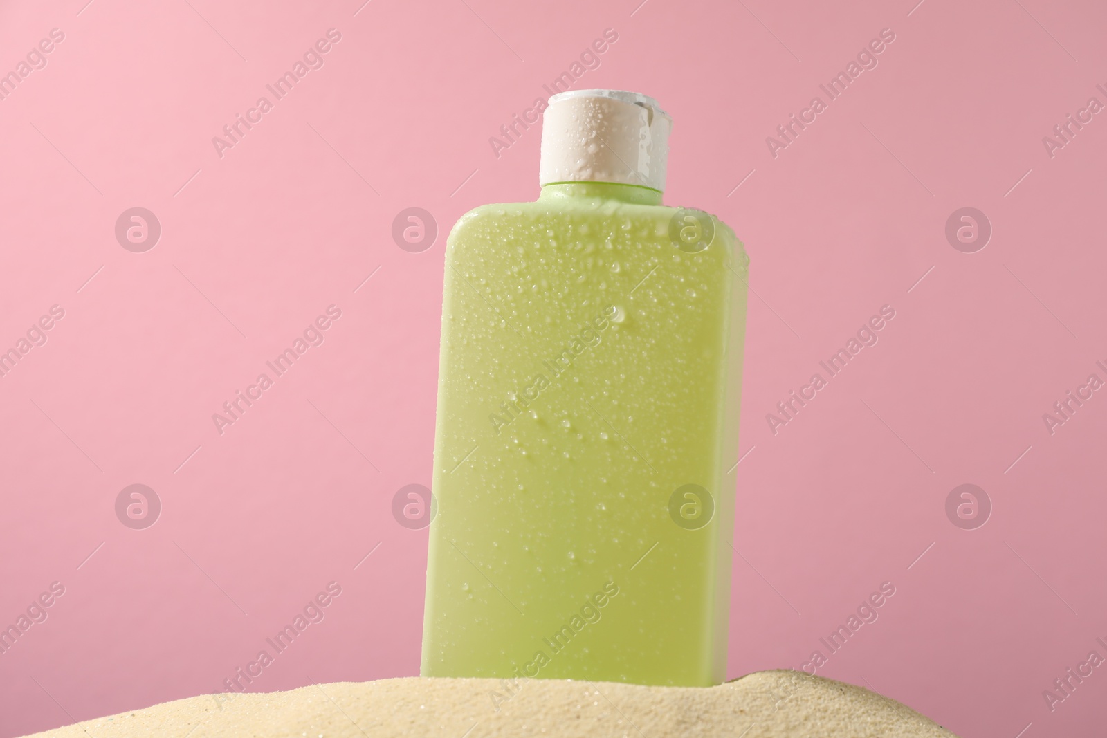 Photo of Bottle of sun protection product on sand against pink background