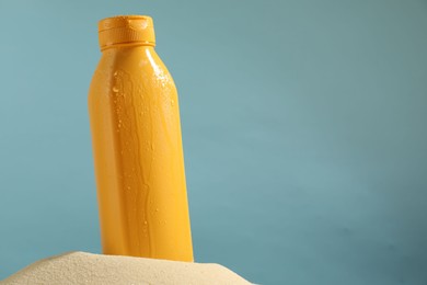 Photo of Bottle of sun protection product on sand against light blue background, space for text