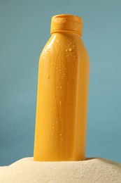 Photo of Bottle of sun protection product on sand against light blue background