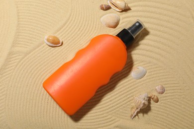 Photo of Bottle of sun protection product and seashells on sand, flat lay