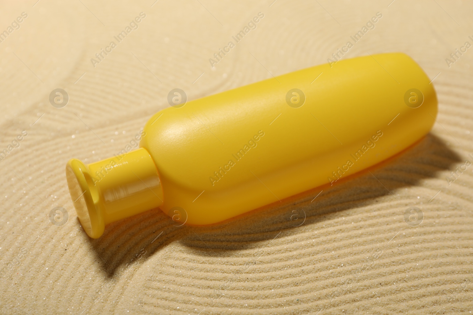 Photo of Bottle of sun protection product on sand, closeup