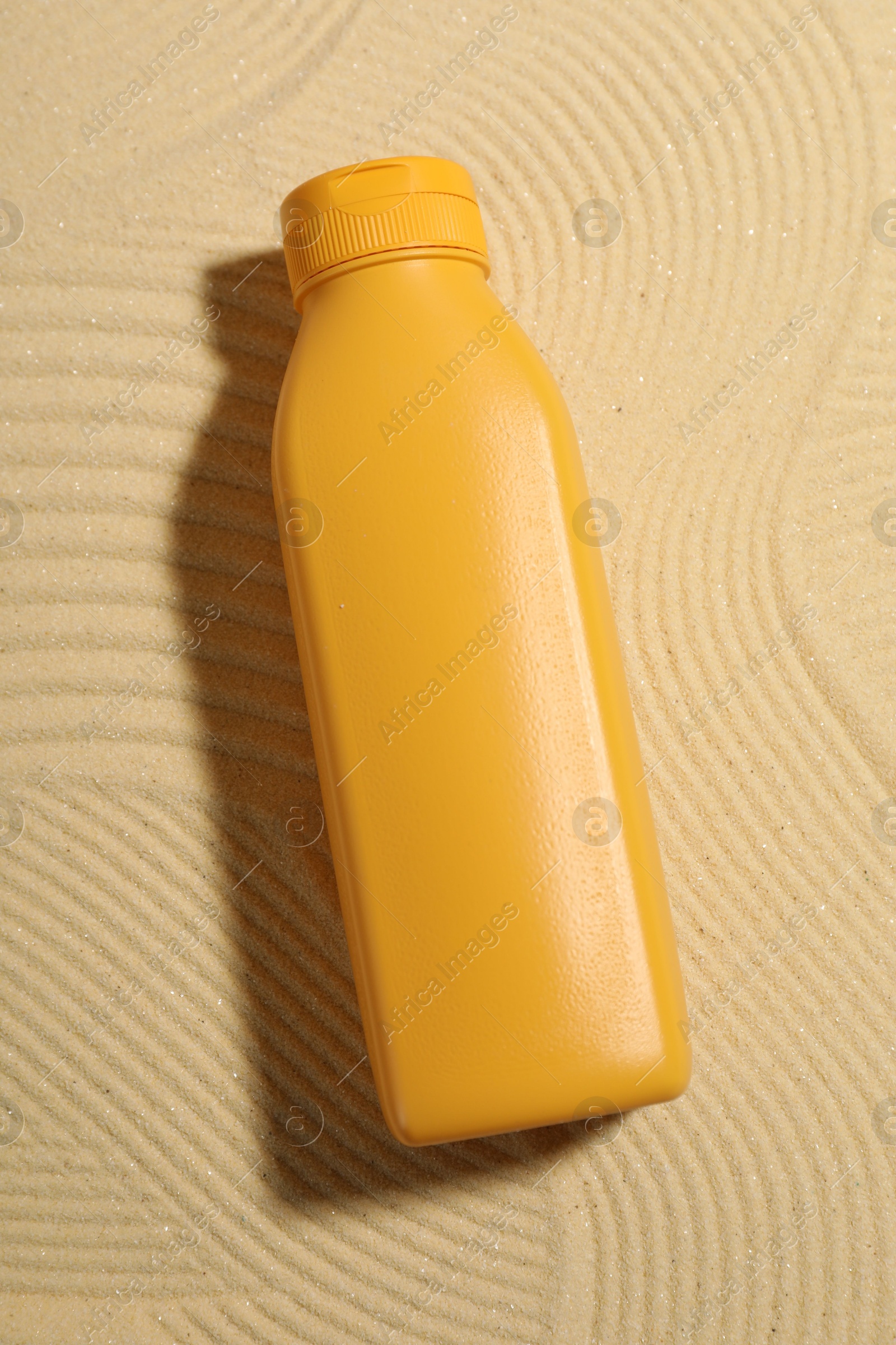 Photo of Bottle of sun protection product on sand, top view