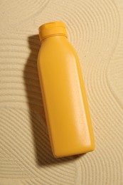 Bottle of sun protection product on sand, top view