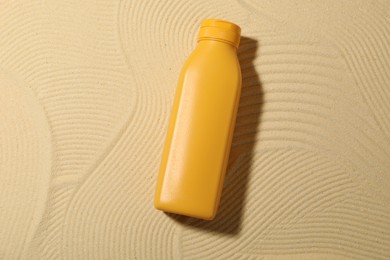 Photo of Bottle of sun protection product on sand, top view