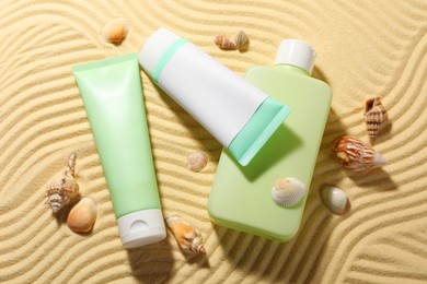 Different sun protection products and seashells on sand, flat lay