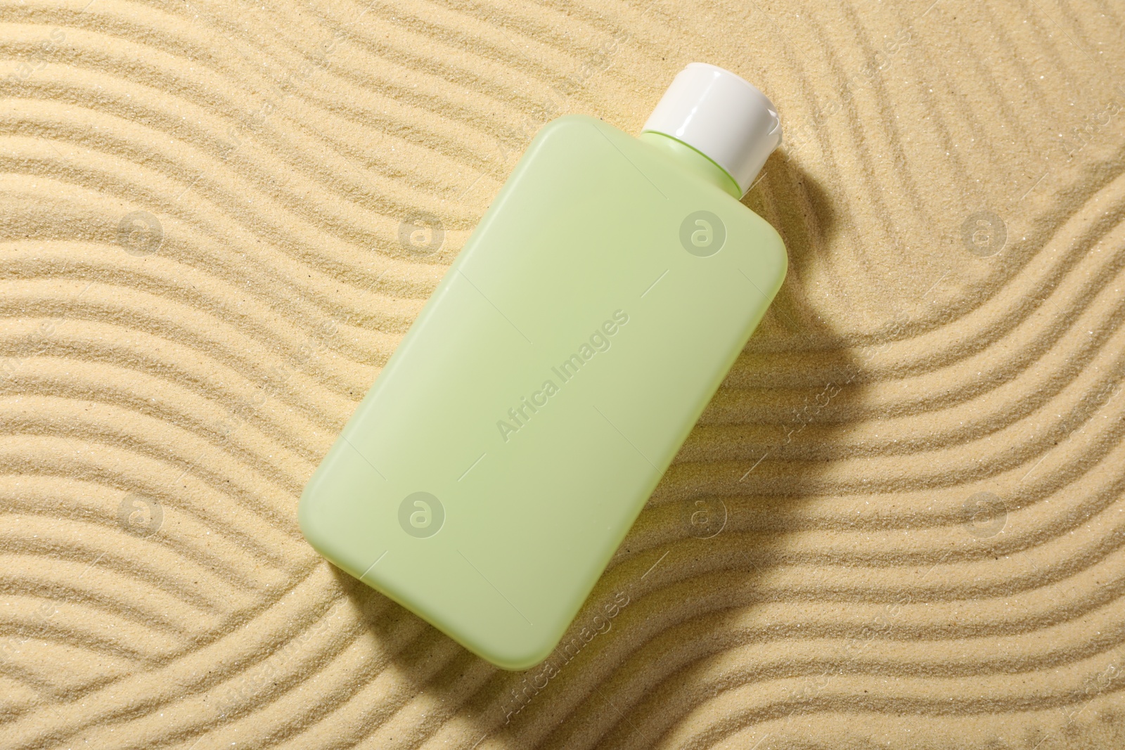 Photo of Bottle of sun protection product on sand, top view