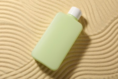 Bottle of sun protection product on sand, top view