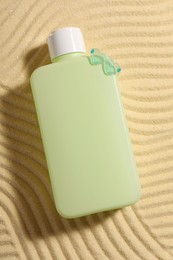 Photo of Bottle of sun protection product on sand, top view